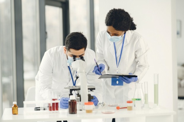 Man Looking at the Microscope with Woman Assistant